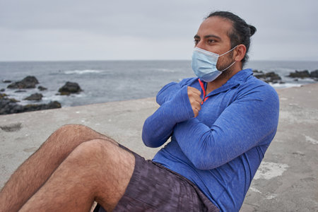 A man with a mask doing sit-ups in front of the sea - new normality, a sports sessionの写真素材