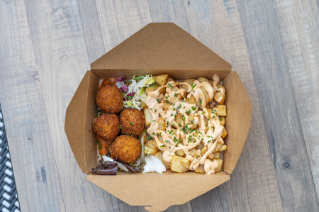 A closeup shot of a box with fries, sauce, and meatballs