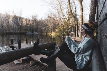 a young woman sitting in front of wooden cabin with a cup of teaの写真素材