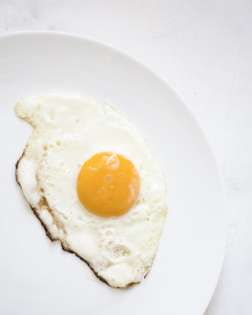 We see a fried egg on a white plate with a white background.の写真素材