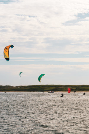 A vertical shot of people kiteboarding at the sea on a sunny day with a cloudy sky aboveの写真素材
