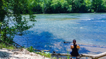 A back view of a female sitting and looking at a blue pondの写真素材