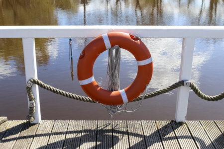 A closeup of a red life ring on a fence of a wooden walkway over a river under the sunlight