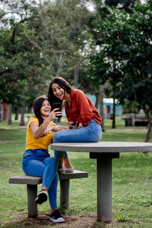 Two attractive cheerful young girlfriends from Argentina laughing at a meme in a parkの写真素材
