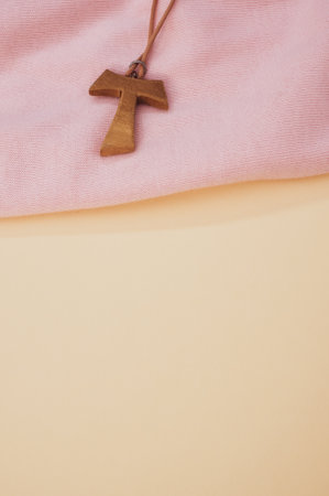 A closeup of a wooden tau cross necklace on a pink cloth and pastel peach surface for a copy spaceの写真素材
