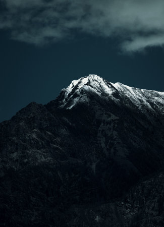 A vertical shot of a rocky mountain covered with snow under a cloudy skyの写真素材