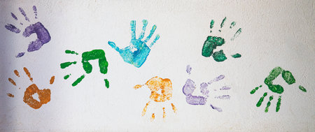 A panoramic shot of colorful handprints on a white wallの写真素材