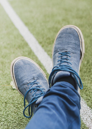A vertical shot of a man wearing blue shoes with crossed legs on grassの写真素材