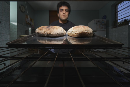 A young Hispanic male baking delicious bread in the oven at homeの写真素材