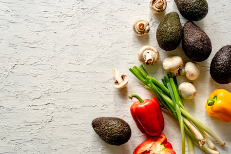A top view of fresh vegetables on a textured white surface with copy space, avocados, mushrooms,...