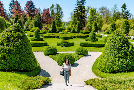 Young woman walking on path in beautiful green park with hedge shapes and trees at Arboretum volcji potok near Radomlje in Slovenia.の写真素材