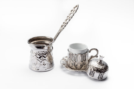 A silver coffee pot with a cup and a pomegranate-shape decoration isolated on a white backgroundの写真素材