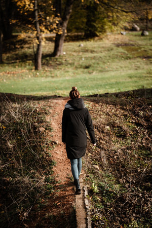 A rear view of a woman wearing a black hoddie coat walking on a path through the meadowの写真素材