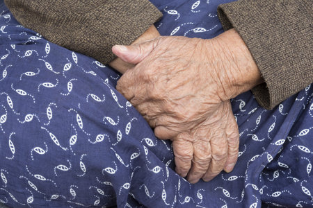 A closeup of the hands of an elderly woman resting on her legsの写真素材
