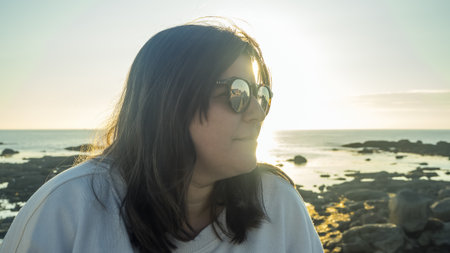 Side close-up of a Caucasian woman wearing sunglasses during a sunset by the sea