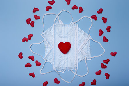 A top view ofvalentine composition of small red hearts on face masks isolated on blue background -...