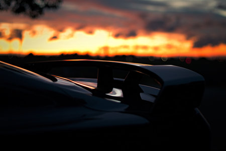 A closeup shot of a black sports car back with a wing against a sunset sky backgroundの写真素材
