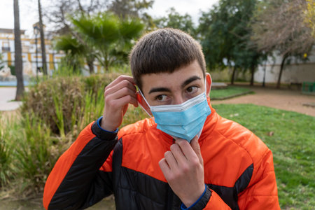 Stock photo of young boy adjusting his face mask in the park.