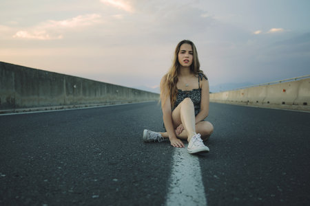 A young attractive Caucasian female posing sitting on a roadの写真素材