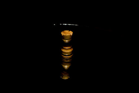 A wooden pawn chess piece with a reflection on black background