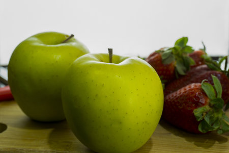 A closeup shot of fresh green apples and strawberries on a chopping boardの写真素材