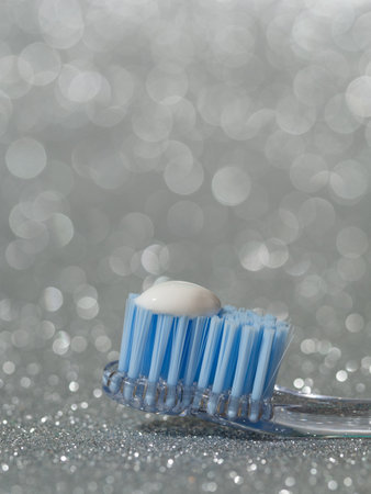 A vertical closeup shot of the head of a blue toothbrush with toothpaste in gray bokeh background