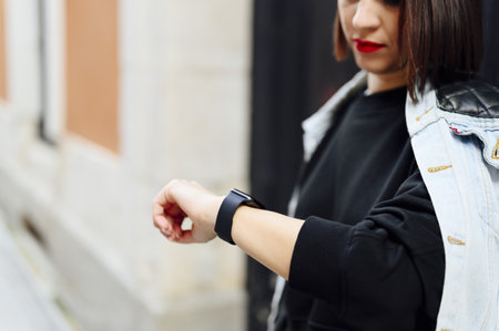 A young attractive female in the casual outfit checking the time while posing on the streetの写真素材