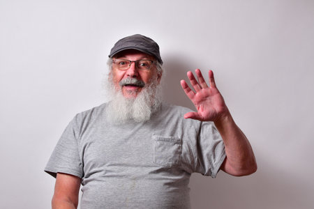 Old American male with a grey shirt and grey gatsby cap waving with one handの写真素材