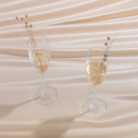 A closeup shot of two glasses of champagne with golden pearls on beige claothの写真素材