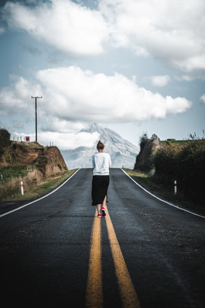 A mesmerizing view of a young tourist walking on the empty road leading to the mountainの写真素材