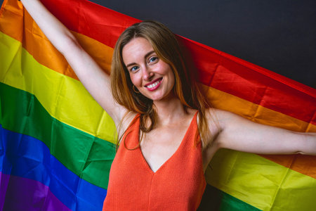 Picture of Smiling Young Adult Blonde Woman Holing Up Rainbow LGTB Flag With Open Arms Over Grey Background Isolated.の写真素材