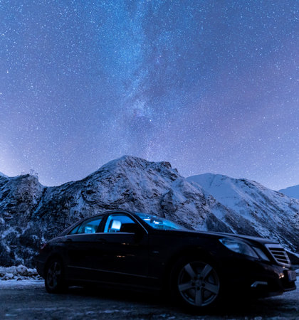 A closeup shot of a black luxury car on the mountains against the Milky Way backgroundの写真素材