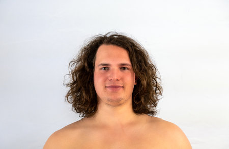 A headshot of a smiling long-haired guy posing shirtless in the light gray studio backgroundの写真素材