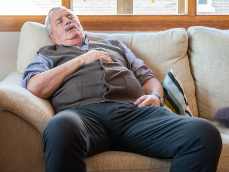 A tired elderly male fall asleep on a comfortable couch in the living roomの写真素材