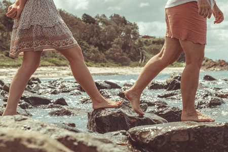 A closeup of a couple of friends enjoying their time by walking on the rocks by the wavy oceanの写真素材