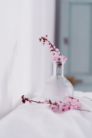 A vertical shot of a glass vase with blossomed cherry branches on the white tableclothの写真素材