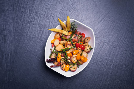 A top view of a salad made with vegetables served in a white plate on a blue tableの写真素材
