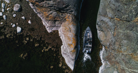 Aerial view above a Boat driving in middle of rocky cliffs, island narrows, in the Finnish archipelago - top down, drone shotの写真素材
