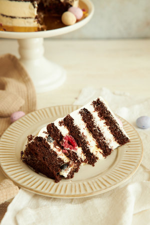 A vertical shot of a piece of a chocolate and raspberry cake with the full one in the background