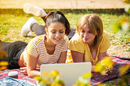 The Two Spanish women lying in the park and looking at a laptop on a sunny dayの写真素材