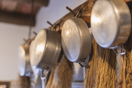 A selective focus shot of a line of steel cooking pans hanging from wooden hangersの写真素材
