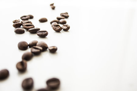 A closeup of the roasted coffee beans scattered on the white surface - space for textの写真素材
