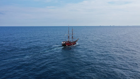 An aerial view of a big sailboat sailing on the wavy ocean under the cloudy blue skyの写真素材