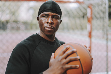 A Black Spanish male in black casual clothes and do-rag holding a basketball ball on an outdoor...