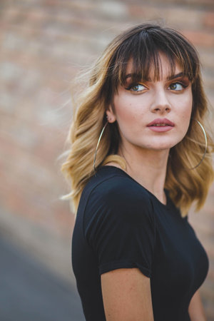 A vertical shot of a Caucasian blond-haired woman with green eyes on the brick wall backgroundの写真素材