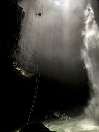 A vertical shot of an extreme hiker climbing down a rope in a cliff