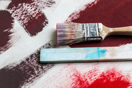 A closeup of a used dirty paintbrush on a paper with red-colored paint brush strokes