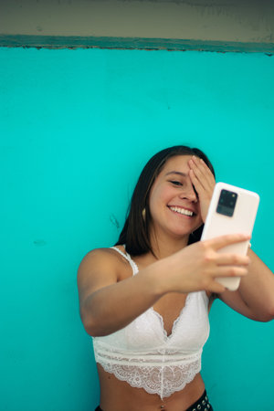 An attractive happy Hispanic female talking via video call near a blue wallの写真素材