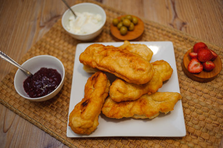 A wooden board with fried zucchini in batter, sauce, jam, and strawberries