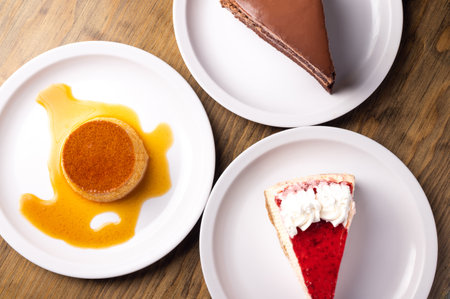 A top view of dessert cakes served in white plates on a wooden surfaceの写真素材